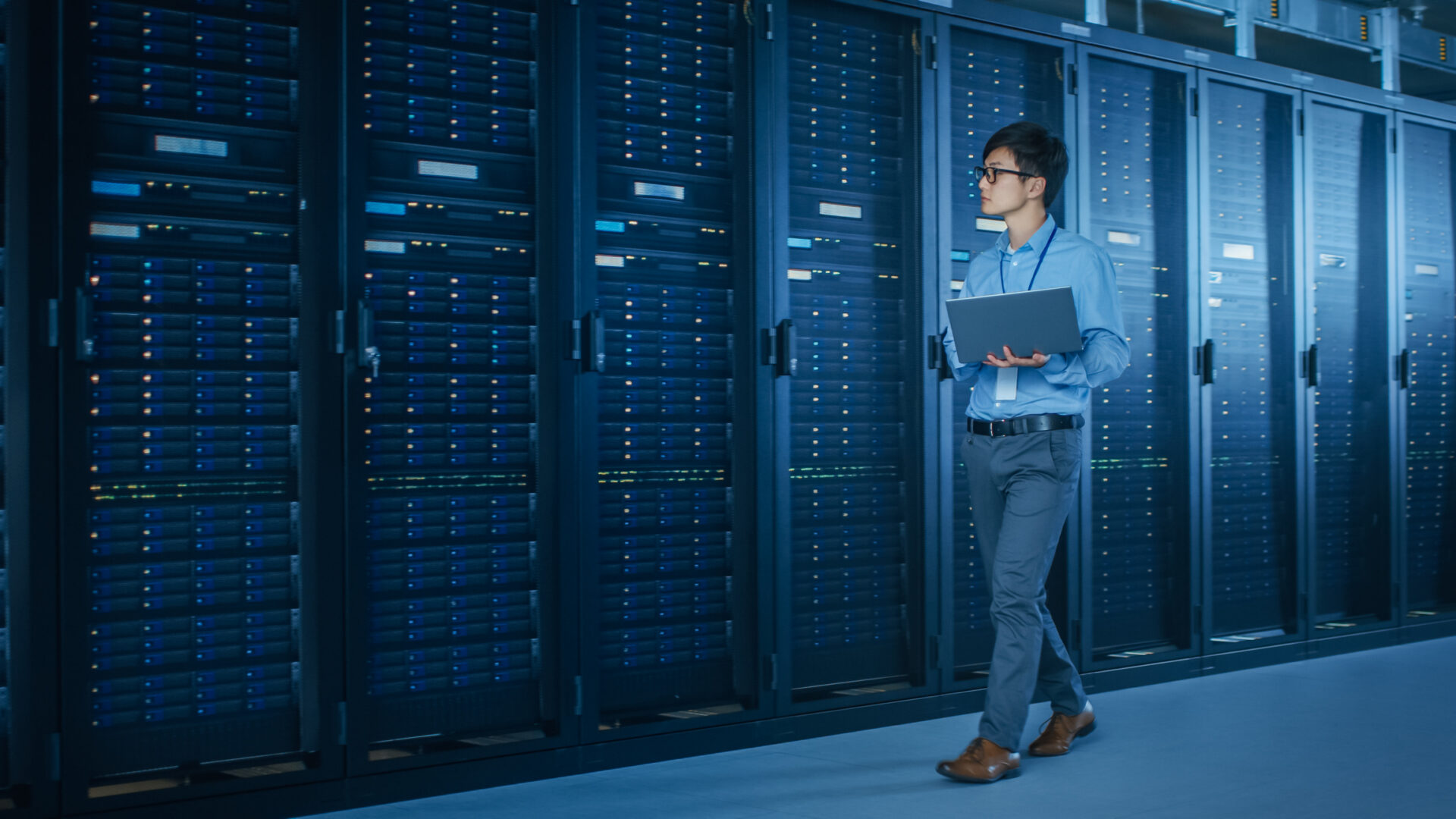 In the Modern Data Center: IT Engineer Working with Server Racks, Uses Laptop for Maintenance and Diagnostics. Checking Stability of the System