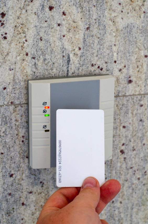 Hand holding an access card near a wall-mounted keypad reader.