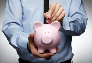 Person in blue shirt putting coin into pink piggy bank.