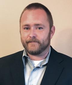 Man with beard wearing a dark blazer and light shirt.