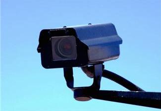 Security camera mounted outdoors against a clear blue sky.