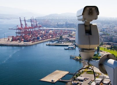 Surveillance camera overlooking a busy port with shipping containers and cranes.