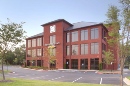 Modern three-story brick office building with large windows and parking area.